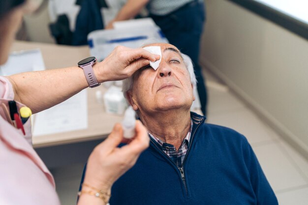 Senior applying eye drops before noninvasive glaucoma laser treatment.